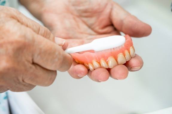 Person cleaning their denture with a toothbrush