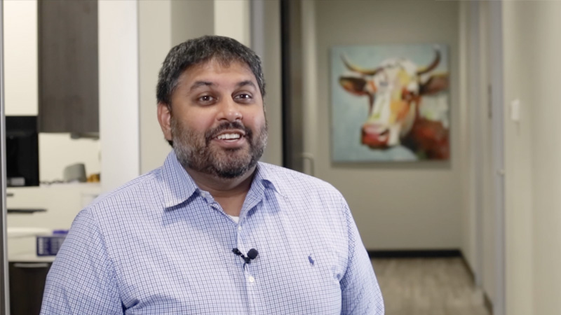 Doctor Desai sitting in dental office hallway with painting of longhorn in background