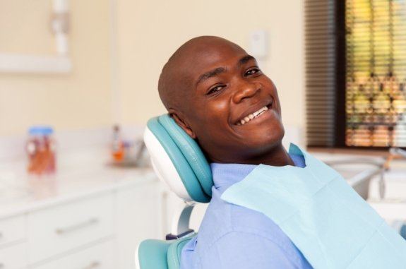 Smiling man in light blue collared shirt leaning back in dental chair