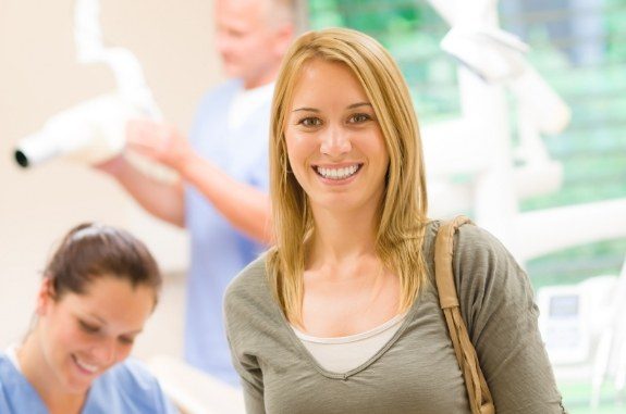 Blonde woman with purse on shoulder smiling in dental office