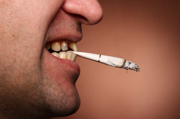 Person holding a partially smoked cigarette between their teeth