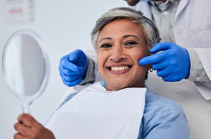 Patient smiling while holding small mirror with dentist