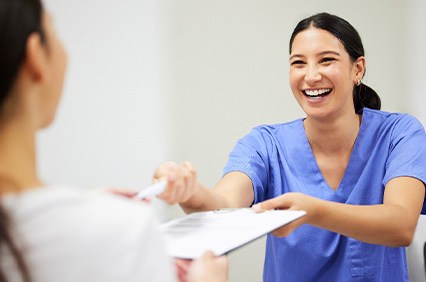 Dental assistant smiling while handing patient form